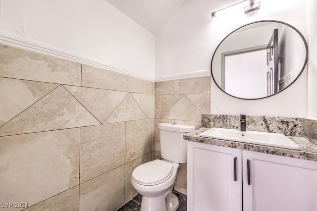 bathroom with vanity, lofted ceiling, toilet, and tile walls