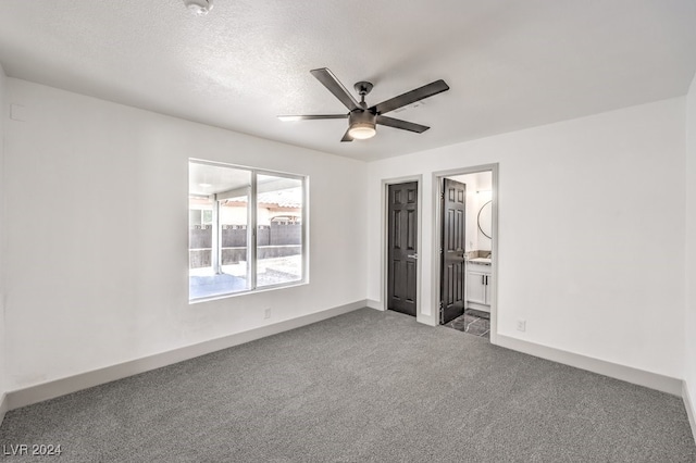 unfurnished bedroom with connected bathroom, ceiling fan, a textured ceiling, and dark colored carpet