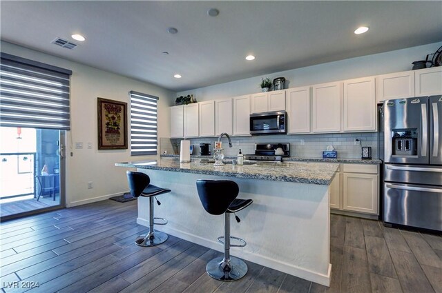 kitchen featuring dark wood-type flooring, appliances with stainless steel finishes, plenty of natural light, and a center island with sink