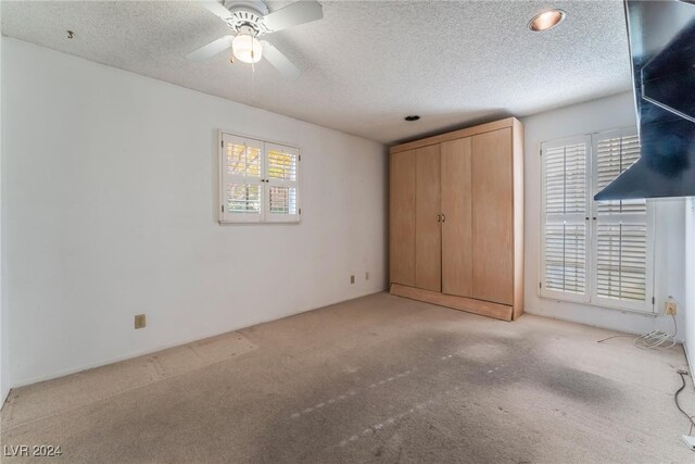 unfurnished bedroom with ceiling fan, light carpet, and a textured ceiling