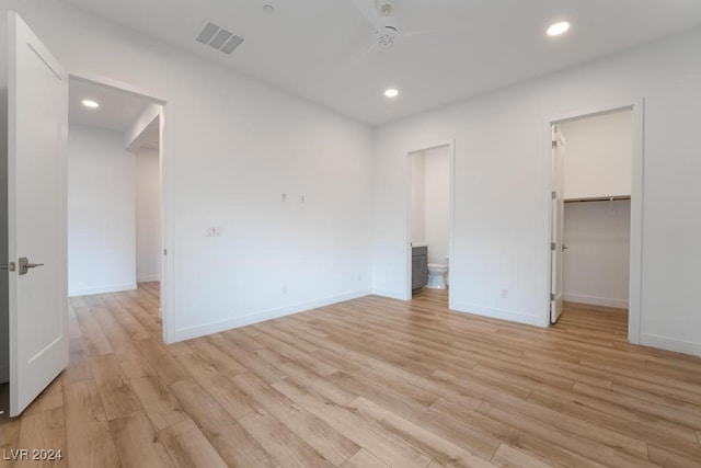 unfurnished bedroom featuring light wood-type flooring, a walk in closet, ensuite bath, a closet, and ceiling fan