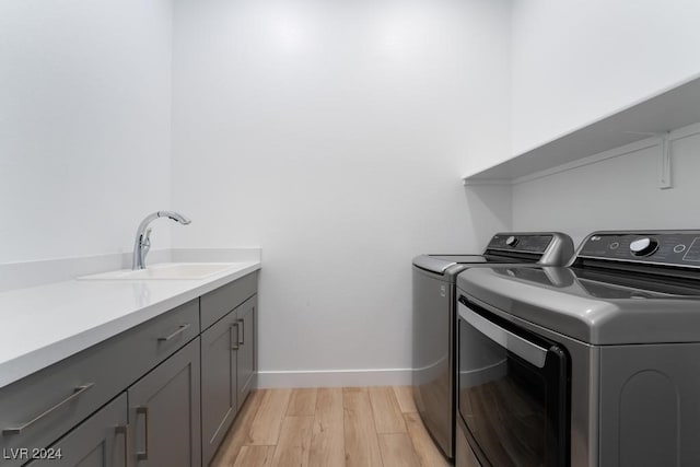 clothes washing area featuring sink, washing machine and dryer, light wood-type flooring, and cabinets