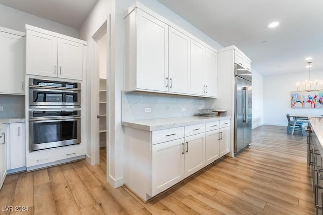 kitchen with decorative backsplash, light hardwood / wood-style flooring, white cabinets, and stainless steel appliances