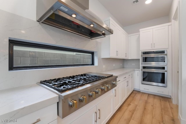 kitchen with light hardwood / wood-style flooring, ventilation hood, light stone countertops, white cabinets, and appliances with stainless steel finishes