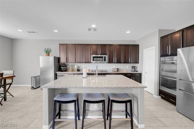 kitchen featuring appliances with stainless steel finishes, dark brown cabinetry, a center island with sink, and a breakfast bar area