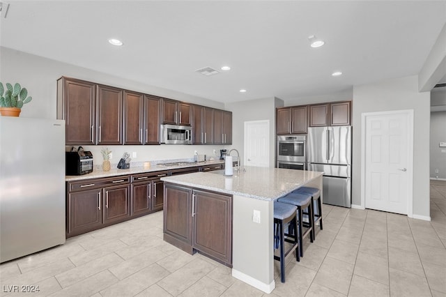 kitchen featuring a breakfast bar, a kitchen island with sink, sink, dark brown cabinets, and stainless steel appliances