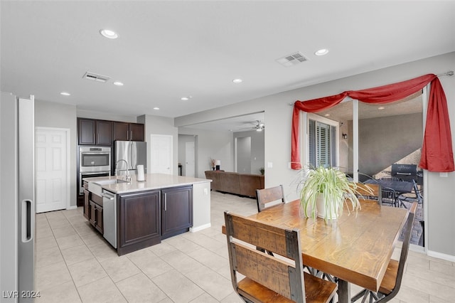 kitchen featuring dark brown cabinetry, ceiling fan, stainless steel appliances, a kitchen island with sink, and light tile patterned floors