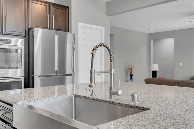 kitchen with sink, ceiling fan, light stone countertops, dark brown cabinets, and stainless steel appliances