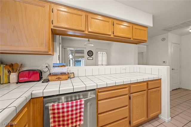 kitchen featuring tile countertops, light tile patterned floors, kitchen peninsula, and dishwasher