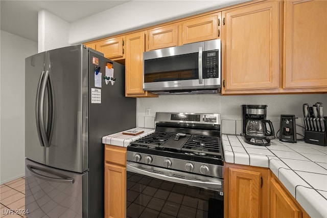 kitchen with tile countertops, stainless steel appliances, light tile patterned floors, and light brown cabinets