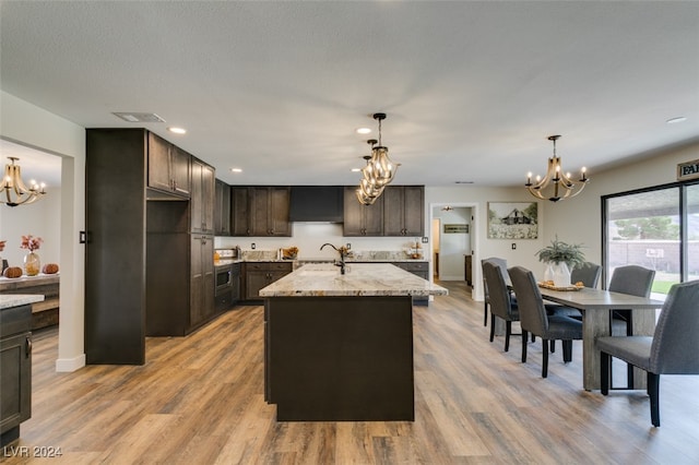 kitchen featuring light stone countertops, dark brown cabinets, light wood-type flooring, and a center island with sink