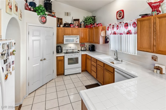 kitchen with light tile patterned flooring, sink, tile countertops, kitchen peninsula, and white appliances