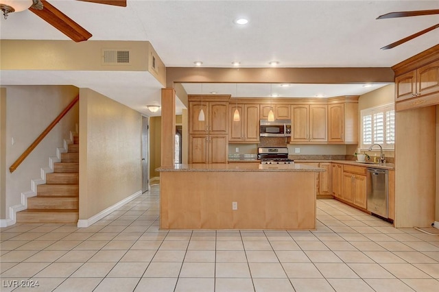 kitchen with light brown cabinetry, stainless steel appliances, light stone counters, and a kitchen island