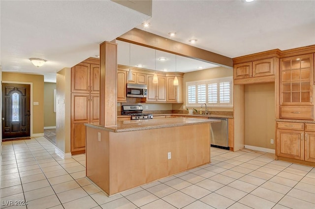 kitchen with sink, light tile patterned floors, appliances with stainless steel finishes, a kitchen island, and light stone counters