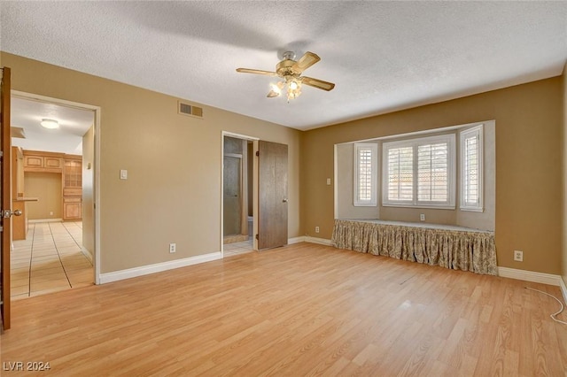 unfurnished bedroom featuring ceiling fan, light wood-type flooring, a textured ceiling, and connected bathroom