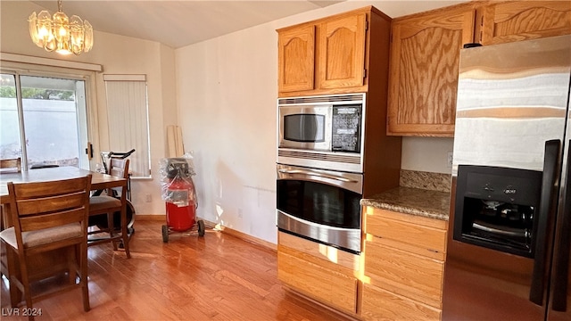 kitchen with stainless steel appliances, wood-type flooring, dark stone countertops, a chandelier, and hanging light fixtures