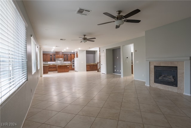 unfurnished living room featuring ceiling fan, light tile patterned floors, and a fireplace