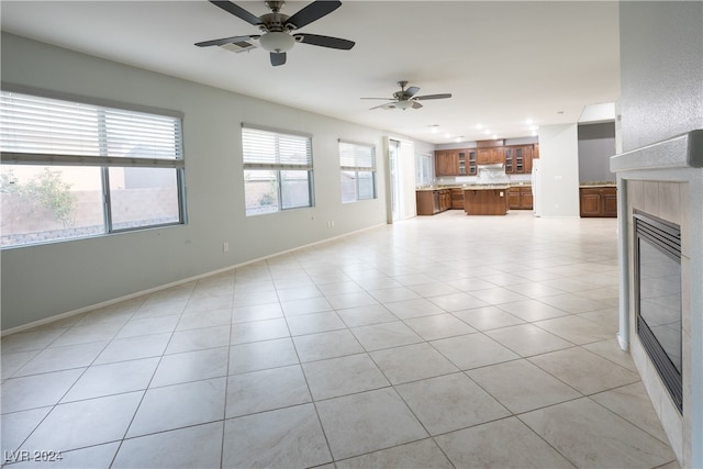 unfurnished living room with ceiling fan, a fireplace, and light tile patterned floors