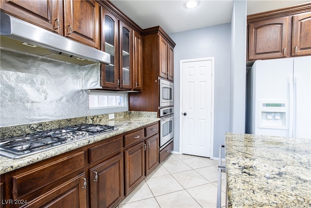 kitchen featuring stainless steel appliances, dark brown cabinets, light stone counters, and light tile patterned floors