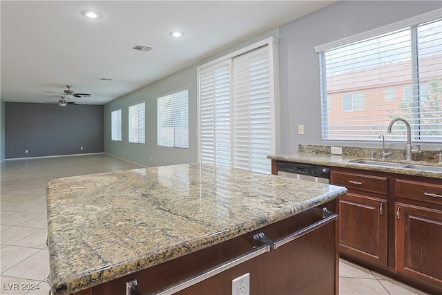 kitchen with ceiling fan, light tile patterned floors, a kitchen island, light stone countertops, and sink