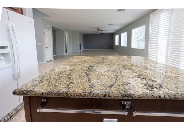 kitchen with stone counters, light tile patterned floors, white refrigerator with ice dispenser, and ceiling fan