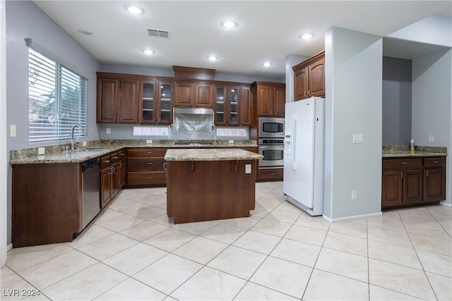 kitchen with light stone counters, appliances with stainless steel finishes, sink, dark brown cabinetry, and a center island