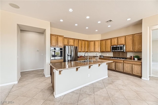 kitchen featuring light tile patterned flooring, sink, a breakfast bar area, appliances with stainless steel finishes, and a kitchen island with sink