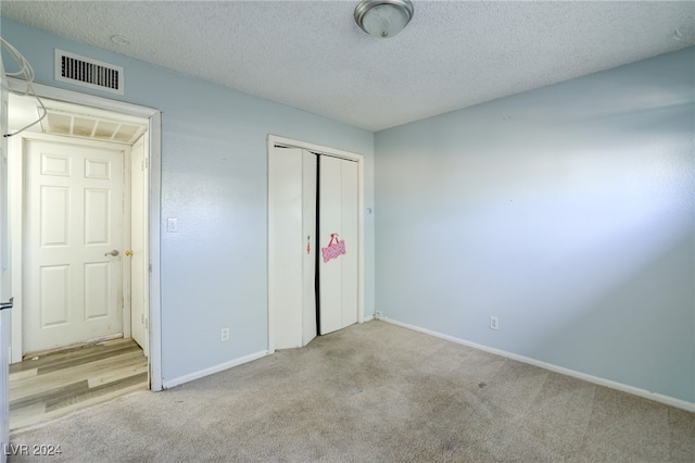 unfurnished bedroom with a closet, a textured ceiling, and light colored carpet