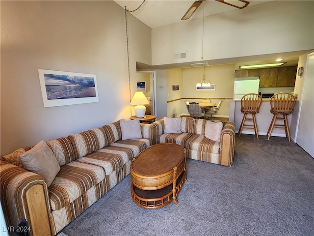 living room with a towering ceiling, ceiling fan, and dark colored carpet