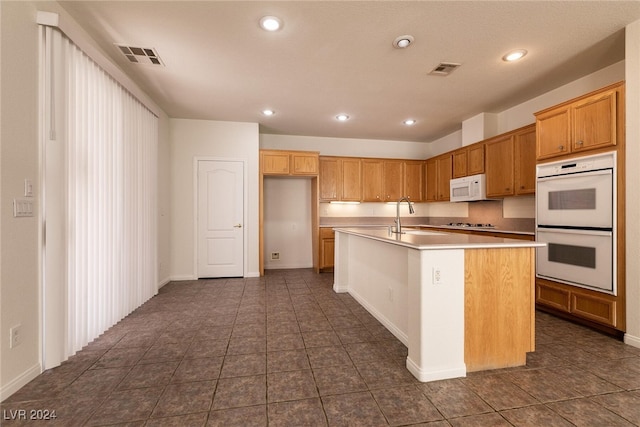 kitchen with a center island with sink, dark tile patterned floors, white appliances, and sink