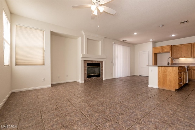 unfurnished living room with ceiling fan, a fireplace, dark tile patterned floors, and sink