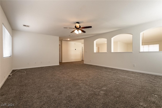 empty room featuring dark colored carpet, ceiling fan, and a healthy amount of sunlight