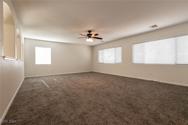 empty room featuring dark colored carpet, ceiling fan, and a healthy amount of sunlight