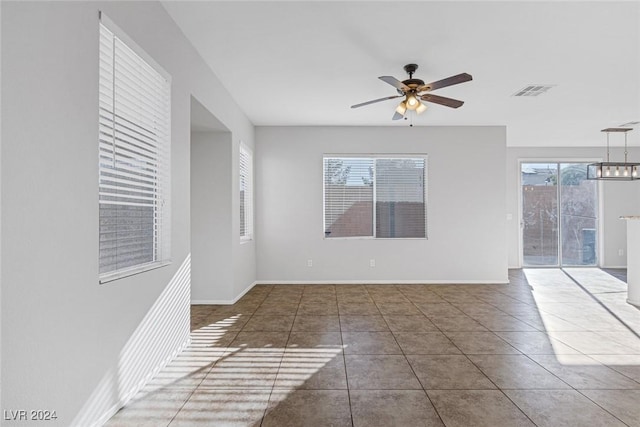 tiled empty room with plenty of natural light and ceiling fan with notable chandelier