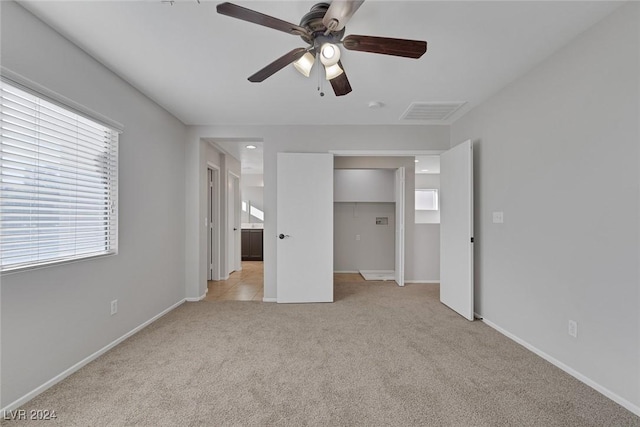 unfurnished bedroom with a spacious closet, light colored carpet, a closet, and ceiling fan