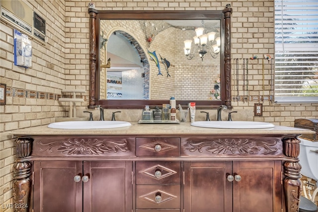 bathroom featuring vanity, a notable chandelier, and brick wall