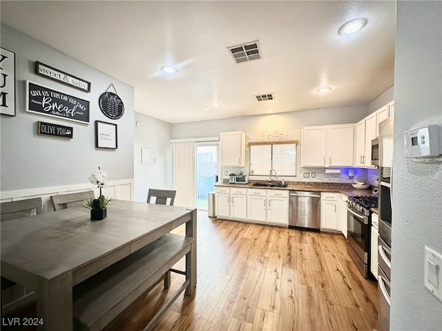 kitchen featuring sink, white cabinets, appliances with stainless steel finishes, light hardwood / wood-style floors, and tasteful backsplash