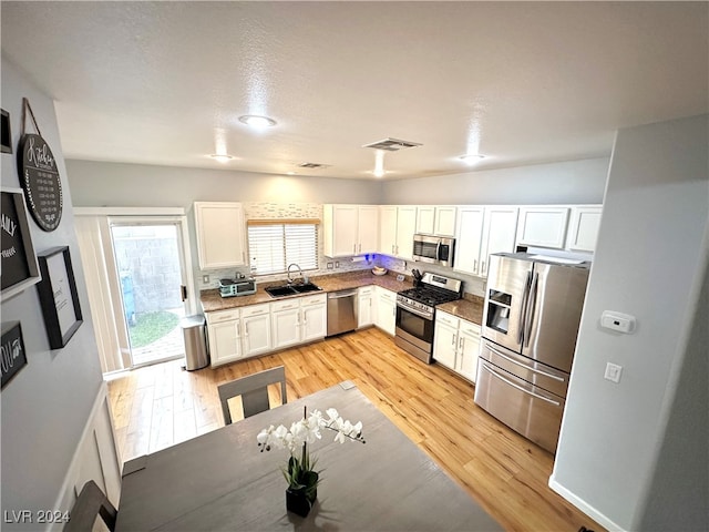 kitchen with vaulted ceiling, appliances with stainless steel finishes, light hardwood / wood-style flooring, and white cabinetry