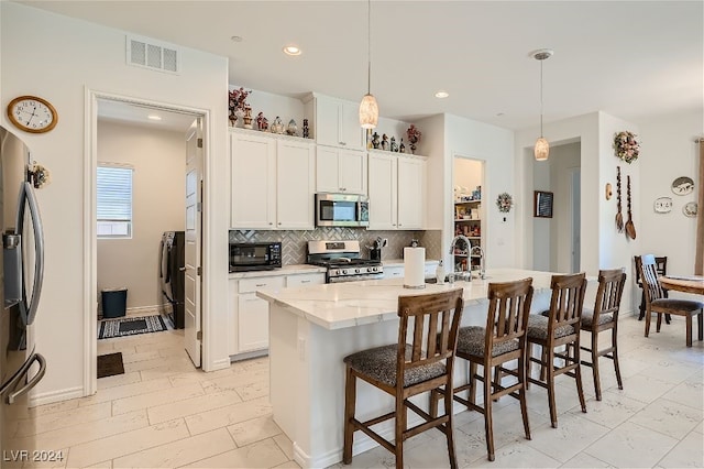 kitchen featuring appliances with stainless steel finishes, decorative light fixtures, an island with sink, and white cabinets