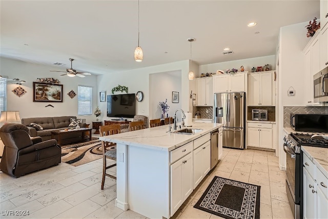 kitchen with sink, white cabinetry, stainless steel appliances, pendant lighting, and a kitchen island with sink