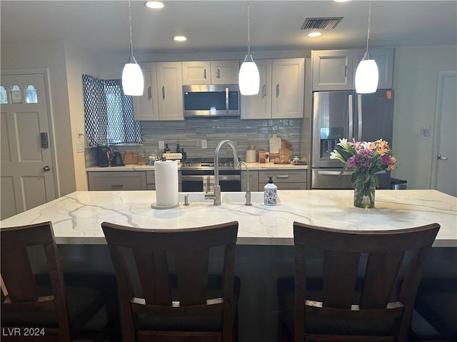 kitchen with a breakfast bar, stainless steel appliances, pendant lighting, and an island with sink