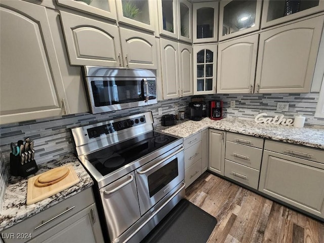 kitchen with decorative backsplash, light stone countertops, dark wood-type flooring, and appliances with stainless steel finishes