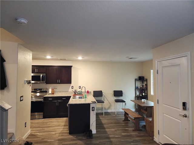 kitchen with kitchen peninsula, dark brown cabinets, stainless steel appliances, sink, and hardwood / wood-style floors