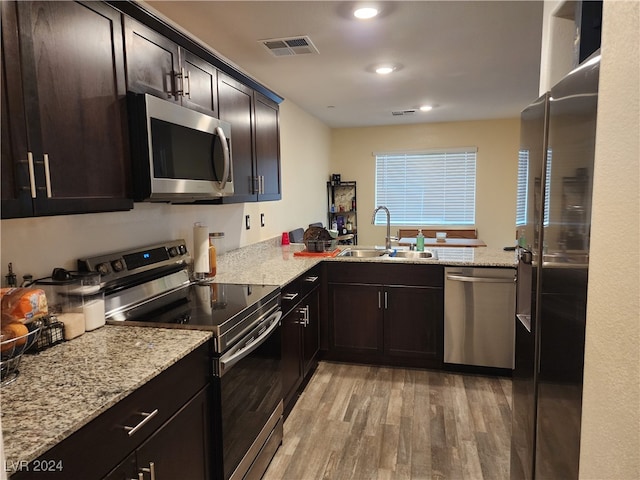 kitchen with sink, appliances with stainless steel finishes, light hardwood / wood-style floors, kitchen peninsula, and light stone counters