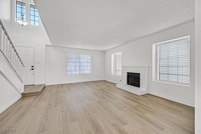 unfurnished living room featuring a brick fireplace, a textured ceiling, and light hardwood / wood-style flooring