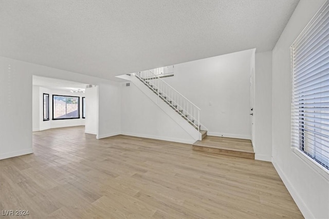 unfurnished living room with light wood-type flooring and a textured ceiling