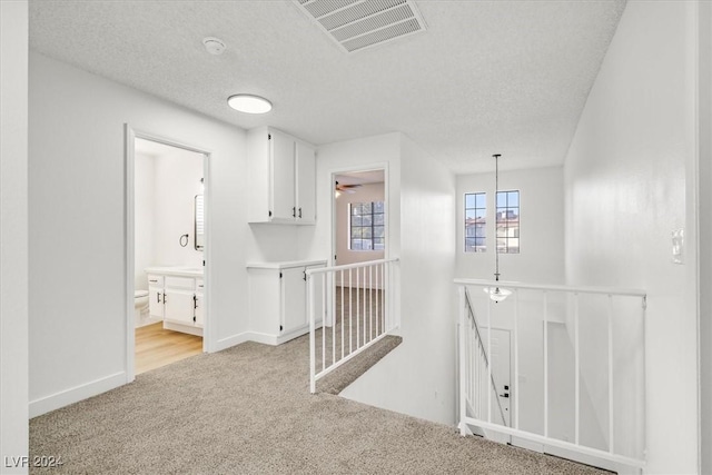 corridor with a textured ceiling and light colored carpet