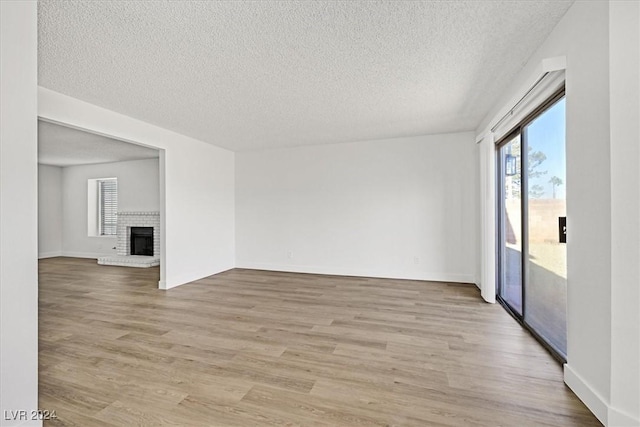 unfurnished room featuring a brick fireplace, a wealth of natural light, and light wood-type flooring