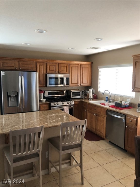 kitchen featuring a kitchen breakfast bar, sink, light tile patterned floors, appliances with stainless steel finishes, and light stone counters