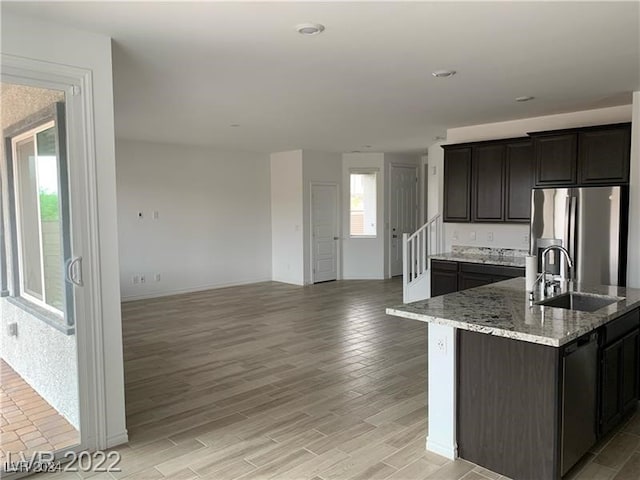 kitchen with light stone countertops, appliances with stainless steel finishes, light wood-type flooring, a kitchen island with sink, and sink